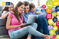 EIne Familie mit zwei Kindern sitzen am Boden und schauen gemeinsam in einen Laptop.