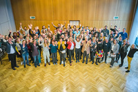 Das Bild zeigt die 60 Teilnehmer/innen der Ring-Tagung. Alle lächeln und halten ihre Arme motivierend in die Höhe.