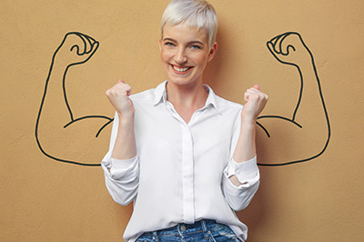 Frau steht vor einem braunen Hintergrund. Auf diesem sind von ihrer Schulter weg, Arme gezeichnet die die Muskeln anspannen, wie ein Bodybuilder. Das Foto soll Motivation und innere Stärke symbolisieren.