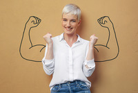 Eine Frau steht vor einer brauen Wand auf der zwei angespannte Arme gezeichnet sind. Diese sollen Stärke vermitteln.