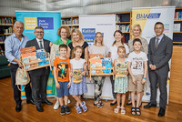 Auf einem Gruppenbild lächeln die Gewinnerkinder des Lesepasses mit ihren Lehrerinnen und Direktorinnen in die Kamera. Sie haben Bücherpakete und Lesesackerl in den Händen. 