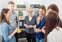 Eine Gruppe junger Frauen und Männer steht in einem Büro zusammen und besprechen etwas.