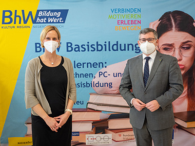Therese Reinel, Geschäftsführerin BhW Niederösterreich GmbH und Ludwig Schleitzko, Landesrat stehen vor einem Werbeplakat der Basisbildung.