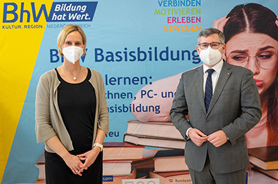 Therese Reinel, Geschäftsführerin BhW Niederösterreich GmbH und Ludwig Schleitzko, Landesrat stehen vor einem Werbeplakat der Basisbildung.