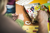 Nahaufnahme von Kinder- und Erwachsnenehänden die in einer Schachtel mit Spielzeug-Buchstaben wühlen.