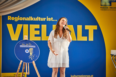 Eine Frau im weißen Kleid steht auf der Bühne und singt in ein Mikrofon.