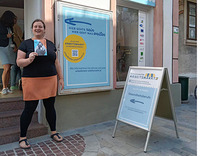 Bildungsberaterin Christa Sieder steht vor dem Schaufenster Arbeitsmarkt in Mödling und hält den Folder der bildungsberatung in der Hand.