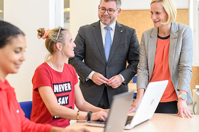 Zwei junge Frauen sitzen am Laptop, Landesrat Schleritzko und BhW Geschäftsführerin Therese Reinel stehen daneben und unterhalten sich mit einer der beiden Damen.