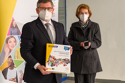 Landesrat Ludwig Schleritzko präsentiert eine Smartphone-Mappe in der Hand, daneben steht eine ältere Dame mit einem Smartphone in der Hand.