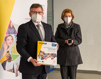 Landesrat Ludwig Schleritzko präsentiert eine Smartphone-Mappe in der Hand, daneben steht eine ältere Dame mit einem Smartphone in der Hand.