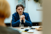 Gehörlosenverband Niederösterreich-Leiter Lukas Huber sitzt an einem Tisch mit Glas, Kaffeegeschirr und Kuchenteller darauf und verschränkt die Hände. Ihm gegenüber und mit dem Rücken zur Kamera sitzt eine Frau mit blondem Haar.