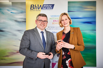 Landesrat Ludwig Schleritzko und BhW Geschäftsführerin Therese Reinel stehen vor einem BhW Rollup und halten jeweils ein Handy in der Hand.