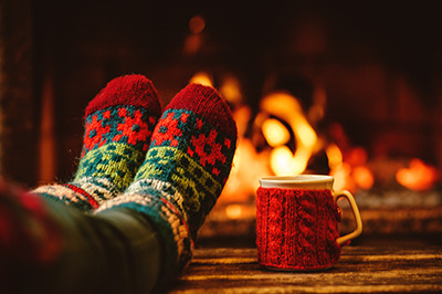 Füße in Wollsocken vor dem Kamin, daneben steht ein Heferl mit einem heißen Getränk.