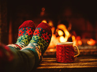 Füße in Wollsocken vor dem Kamin, daneben steht ein Heferl mit einem heißen Getränk.