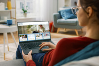 Eine Frau sitzt auf der Couch, hat einen Laptop am Schoss und schaut in die Bildungsdatenbank NÖ.