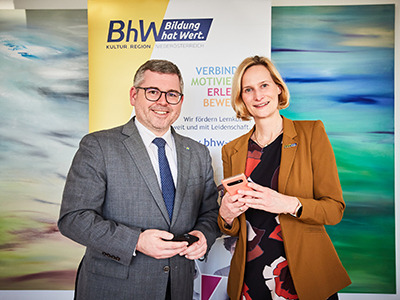 Landesrat Ludwig Schleritzko und BhW Geschäftsführerin Therese Reinel stehen vor einem BhW Rollup und halten jeweils ein Handy in der Hand.