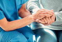 Die Hände einer Person in Pflegeberufs-Kleidung halten die Hände einer anderen Person, die wahrscheinlich von ihr betreut wird.