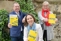 Drei Personen, ein Mann, zwei Frauen, halten jeweils eine gelbe Broschüre in der Hand. 