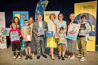 Gruppenbild, in der ersten Reihe stehen Kinder und in der zweiten Reihe Erwachsene Personen. Im Hintergrund stehen einige Rollups vom BhW, Zeit Punkt Lesen und Kulturregion.