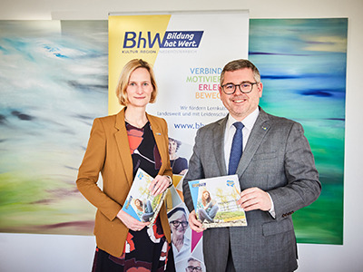 Landesrat Ludwig Schleritzko und BhW Geschäftsführerin Therese Reinel stehen vor einem BhW Rollup und halten die Broschüre "Bildungsagenda NÖ" in den Händen.