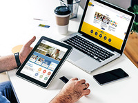 Männerhände halten ein Tablet auf dem die Startseite von https://www.bildungsangebote.at zu sehen ist. Dahinter steht ein Laptop auf einem Schreibtisch, auf diesem sieht man die Startseite der Homepage https://www.bildungsgemeinden-noe.at
