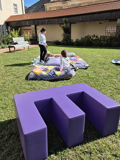Kinder lesen, davor liegt ein Riesenbuchstabe im Gras