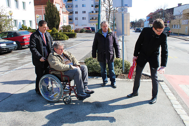 Vier Personen besichtigen einen Fußgängerübergang auf Barrierefreiheit. Ein Mann sitzt im Rollstuhl.