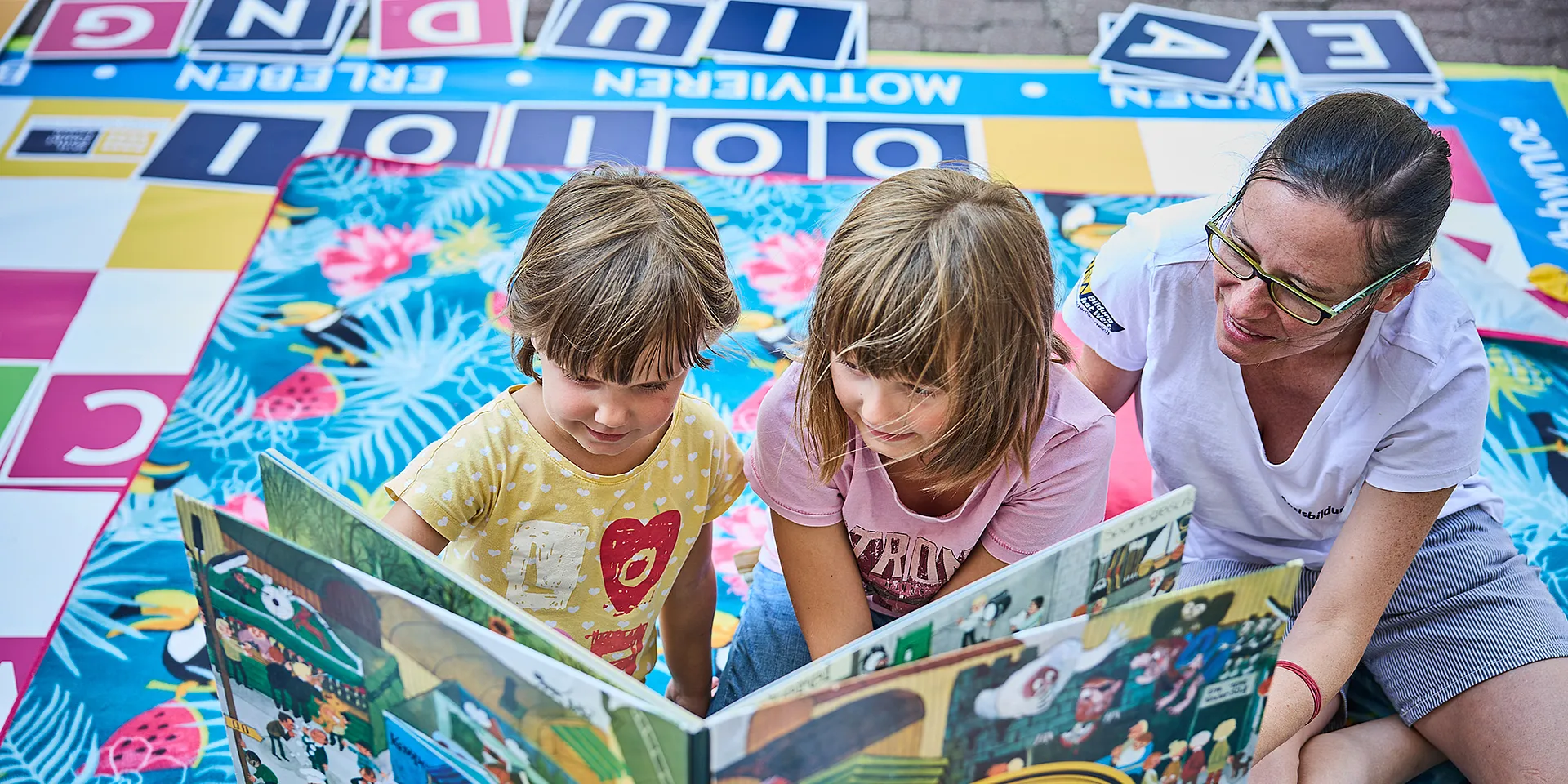 Zwei Kinder und einen Erwachsenen sitzen am Boden und lesen in einem Buch