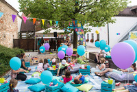 Kinder sitzen auf Decken und Pölter im Park und lauschen einer Geschichte.