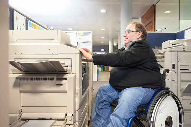 Ein Mann im Rollstuhl versucht auf einem Kopiergerät etwas zu kopieren.