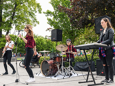 Eine Band mit jungen Musikerinnen und einem Musiker spielen voller Freude in einem Park auf ihren Musikinstrumenten.