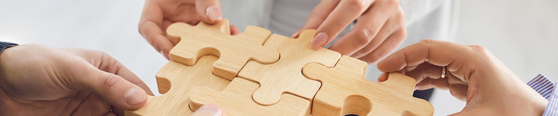 Das Bild die Hände mehrerer Personen, die gemeinsam Puzzle-Teile aus Holz zusammenfügen.