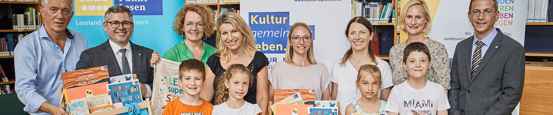 Auf einem Gruppenbild lächeln die Gewinnerkinder des Lesepasses mit ihren Lehrerinnen und Direktorinnen in die Kamera. Sie haben Bücherpakete und Lesesackerl in den Händen. 